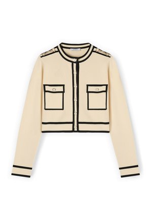 Gekürzter Cardigan in Creme mit schwarzem Besatz, ausgestattet mit zwei vorderen Taschen und goldenen Schulterakzenten. Knopfverschluss vorne mit runder Ausschnitt.