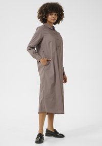 Ilga, ruda, su sagutėmis užsegama suknelė su apykakle, ilgomis rankovėmis ir šoninėmis kišenėmis; pagaminta iš lygaus audinio, su laisvu siluetu.