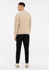 Felpa in pile beige con scollo rotondo e spalle basse, abbinata a pantaloni neri e sneakers beige, su sfondo bianco.