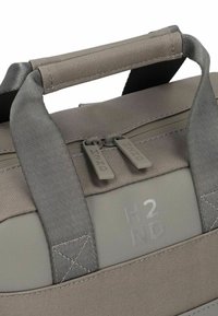 Bolsa de viaje gris con tejido texturizado, tiradores dobles de cremallera, asas reforzadas y logotipo en relieve. Presenta un diseño robusto para mayor durabilidad.