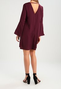 Burgundy klänning med klockärmar, V-ringning, mjukt tyg och lös passform, kombinerad med svarta klacksandaler.