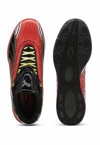 Sneaker rossi e neri con un design lucido, parte superiore testurizzata, dettagli bianchi, lacci gialli e una suola in gomma nera con motivo.