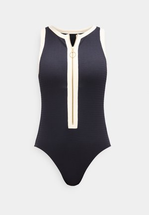 Body in nero senza maniche con bordo bianco e cerniera dorata frontale con tirante circolare, tessuto a costine.