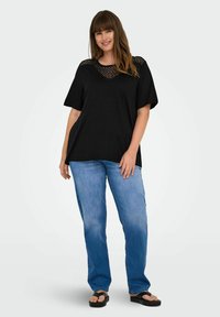 Svart kortärmad topp med ett genomskinligt spetsdetalj vid halsringningen, ihop med blå raka jeans och svarta flip-flops.