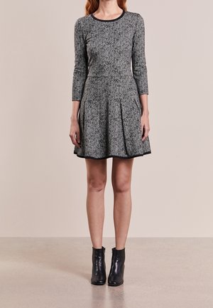 Vestido de pata de gallo gris con mangas largas, falda plisada y ribete negro. Se lleva con botines negros. Textura suave y diseño ajustado.