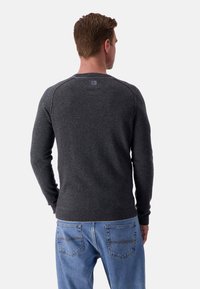 Grauer Strickpullover mit langen Ärmeln und geripptem Saum, kombiniert mit blauen Jeans. Hat ein Etikett auf der Rückseite mit einem Logo.