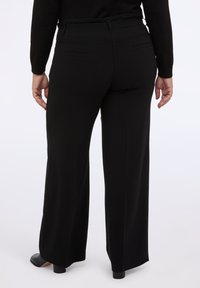 Czarne spodnie szerokie w nogawkach, wykonane z gładkiego materiału, z wysokim stanem, dwiema tylnymi kieszeniami i prostym krojem sięgającym do kostek.
