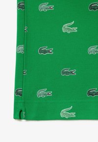 Tissu vert vif avec plusieurs petits logos de crocodiles brodés en vert foncé et blanc, avec des bouches ouvertes rouges.