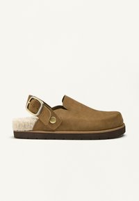 Hnedé semišové dreváky so zateplením z ovčej vlny, otvorenou pätou a striebornou nastaviteľnou prackou. Obsahujú hrubú, textúrovanú podrážku pre pohodlie.