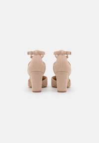 Nude semišové lodičky na vysokém podpatku s kulatou špičkou, kotníkovým páskem a blokovým podpatkem. Zadní pohled ukazuje čistý, minimalistický design.