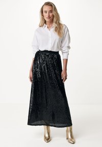 Schwarzer, paillettenbesetzter Maxirock mit gerafftem Bund, kombiniert mit einem weißen Hemd mit Knöpfen. Das Model trägt metallic goldene Blockabsatzstiefel.