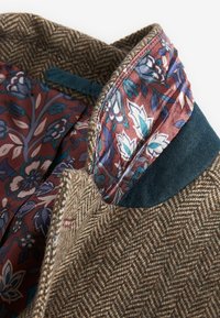 Brun hørmannet tweedjakke med krave og blomster mønstret foer i marmor, blå og hvid, med blå fløjlstrim på kanten.