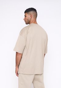 Camiseta de algodón beige de corte grande con mangas cortas, escote redondo y un ajuste relajado, vista desde la parte de atrás. Textura suave y diseño minimalista.