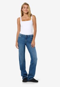 Body alb cu guler pătrat, blugi drepti albastre, țesătură de denim, design simplu, purtat cu adidași negri, modelul posedând cu mâinile pe lângă corp.