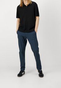 Černé žebrované polo tričko s límečkem, spárované s námořnickými modrými zúženými kalhotami a černými teniskami s bílými pruhy.