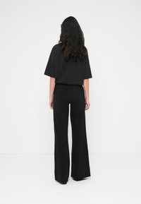 Μαύρο υπερμεγέθες μπλουζάκι και μαύρο τζιν με φαρδιά πόδια. Ομαλό ύφασμα, άνετη εφαρμογή. Ορατή ραφή και δύο πίσω τσέπες στο τζιν.