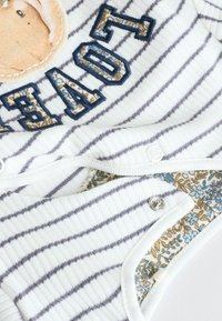 Wit en grijs gestreepte baby romper met geborduurde tekst "LOVED" en een bloemenpatroon stof aan de binnenvoering. Drukknopen aan de onderkant.