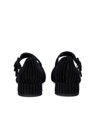 Zapatos de ante negros con una textura acanalada, que presentan un diseño de tira en el talón y un pequeño tacón grueso. Decorados con un detalle de lazada en la parte trasera.