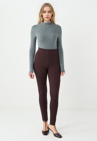 Brązowe legginsy z wysokim stanem o gładkiej tkaninie i detalami szwów, w połączeniu z dopasowaną szaro-skalną bluzką z długim rękawem. Oba elementy są obcisłe.