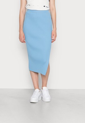 Saia midi azul clara com pregas e bainha diagonal, combinada com ténis brancos, desenhada com uma silhueta ajustada e material elástico.