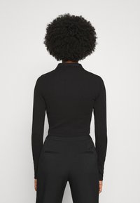 Schwarzes Longsleeve-Polohemd mit Kragen, taillierte Passform, gerippte Textur und leicht cropped Länge, kombiniert mit hochtaillierten schwarzen Hosen.