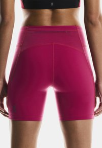 High-waisted, form-fitting shorts in bright pink, featuring a smooth texture and flatlock seams, with a logo in the lower left corner.