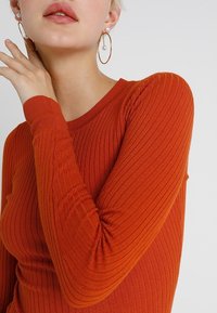 Top a maniche lunghe a coste di un arancione vivace, con scollo tondo e taglio aderente, realizzato in tessuto elasticizzato e strutturato.