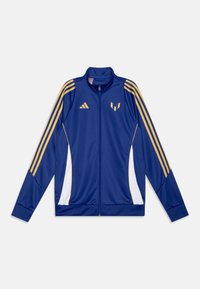 Blauwe ritsjack gemaakt van gladde stof, met gouden strepen op de schouders en zijkanten, witte accenten en een logo op de borst.