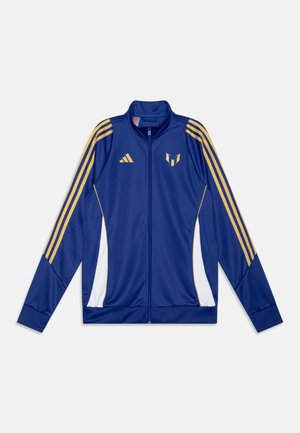 Blauwe ritsjack gemaakt van gladde stof, met gouden strepen op de schouders en zijkanten, witte accenten en een logo op de borst.