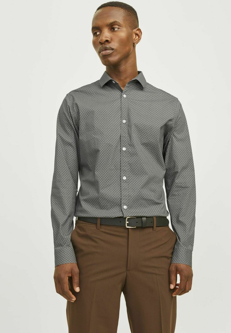 Chemise boutonnée gris foncé avec un motif géométrique, manches longues et un col structuré, associée à un pantalon marron et une ceinture noire.