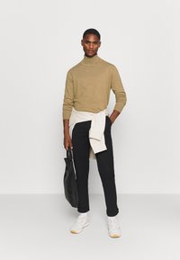 Beige turtleneck sweater, marineblå bukser, hvide sneakers og en sort tote bag. Laget med en lys sweater bundet om taljen.