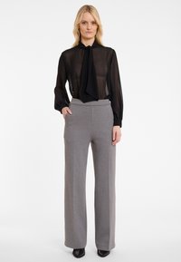 Zwarte doorzichtige blouse met een halsstrik, gecombineerd met grijze hoge taille, wijde broek met verticale streepjes en zakken.