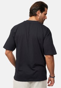 Schwarzes Kurzarm-T-Shirt aus Baumwolle mit Rundhalsausschnitt und lockerer Passform, von hinten gezeigt. Einfaches Design, ohne Muster oder Akzente.