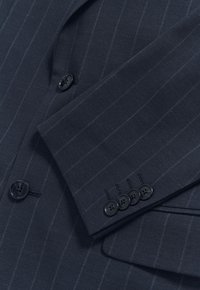 Giacca da abito blu navy con motivo a righe sottili, bottoni neri, una tasca singola e tessuto strutturato. Dettaglio dei bottoni sul polsino.