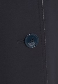 Tissu foncé avec un bouton en plastique noir à quatre trous cousu à côté d'une boutonnière sur une couture.