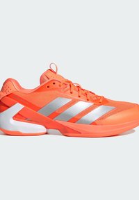 Νεον πορτοκαλί αθλητικό παπούτσι με ασημένιες ρίγες, διχτυωτό πάνω μέρος, μαξιλαρωμένη κολάρα και λευκή σόλα με ξεχωριστό γεωμετρικό σχέδιο.