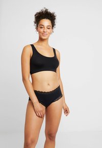 Svart sömlös bralette med breda band, som matchas med svarta hipsterunderbyxor med spetskant. Mjuk tyg, slät textur, minimalistisk design.