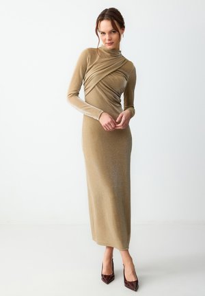 Robe longue et ajustée en tissu doré brillant avec un col montant, un design drapé sur la poitrine et des manches longues.