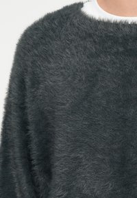Tmavo sivý, chlpatý pletený sveter s voľným strihom, okrúhlym výstrihom a mäkkou textúrou. Tkanina pôsobí teplo a má mierne perleťový vzhľad.
