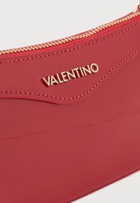 Clutch em pele envernizada vermelha com design ondulado, logótipo "Valentino" em tom dourado e fecho de correr dourado. Textura lisa e brilhante.