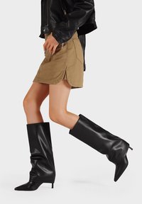 Botas negras hasta la rodilla hechas de cuero suave, con punteras afiladas y talones stiletto ligeros, con un diseño holgado que se extiende por encima de la pantorrilla.