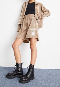 Beige shorts with an elastic waistband and Adidas branding, paired with a black top and black lace-up ankle boots with chunky soles.