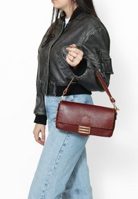 Sac à main en cuir rouge avec une finition texturée, quincaillerie dorée et un design cousu. Il possède une bandoulière amovible et une forme rectangulaire.