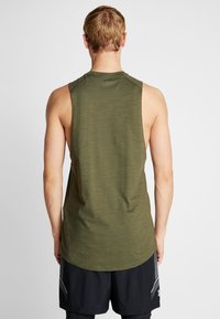 Camiseta atlética verde sin mangas con cuello redondo y tejido texturizado, combinada con pantalones cortos negros que presentan un patrón geométrico en un lado.