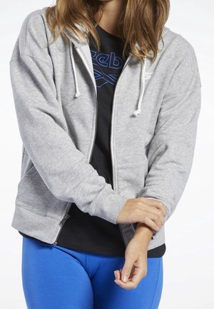Felpa grigia con zip e cordini, dalla texture morbida, con due tasche laterali, indossata sopra una maglietta nera e abbinata a leggings blu.