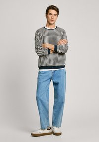 Suéter de algodón a rayas en navy y blanco, combinado con jeans azul claro. Presenta puños y dobladillo acanalados, con zapatos blancos.