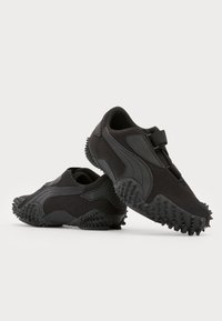Zapatillas deportivas negras con tejido texturizado, que cuentan con acentos de goma, suelas flexibles y una parte inferior única con tachuelas para mayor tracción.