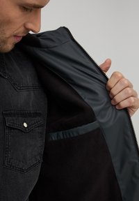 Giacca in denim nero con apertura a zip, dotata di un morbido rivestimento interno in fleece nero e una tasca interna con finitura lucida.