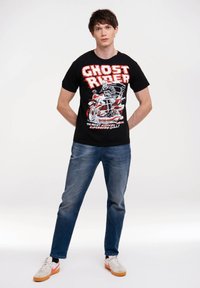 Black cotton t-shirt featuring a graphic print of a motorcycle rider with "GHOST RIDER" text in red. Paired with blue denim jeans and sneakers.