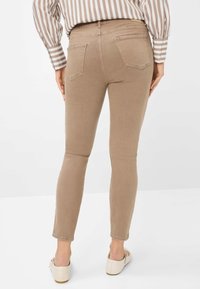 Jeans skinny marrone chiaro in denim, con un design attillato, tasche posteriori standard e cuciture sottili. Abbinati a scarpe di colore chiaro.